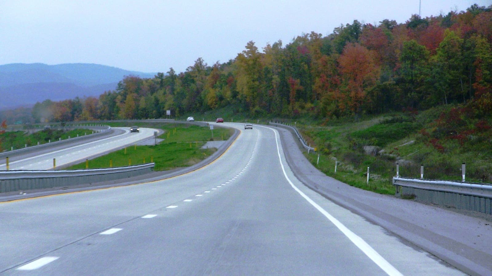 A divided highway curving past a hillside of orange, red and green trees