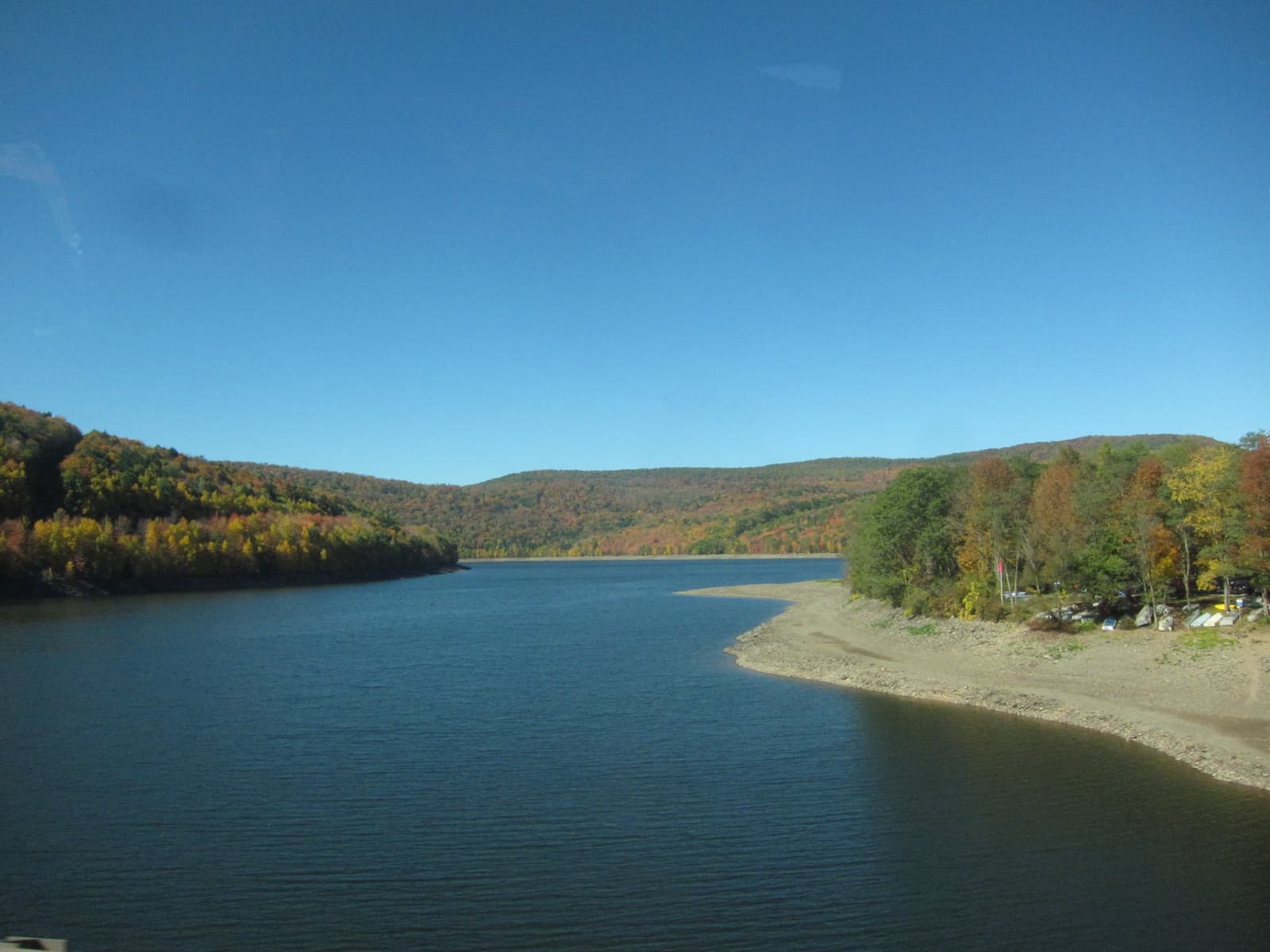 A reservoir winding between hills covered in orange and yellow trees under a clear blue sky