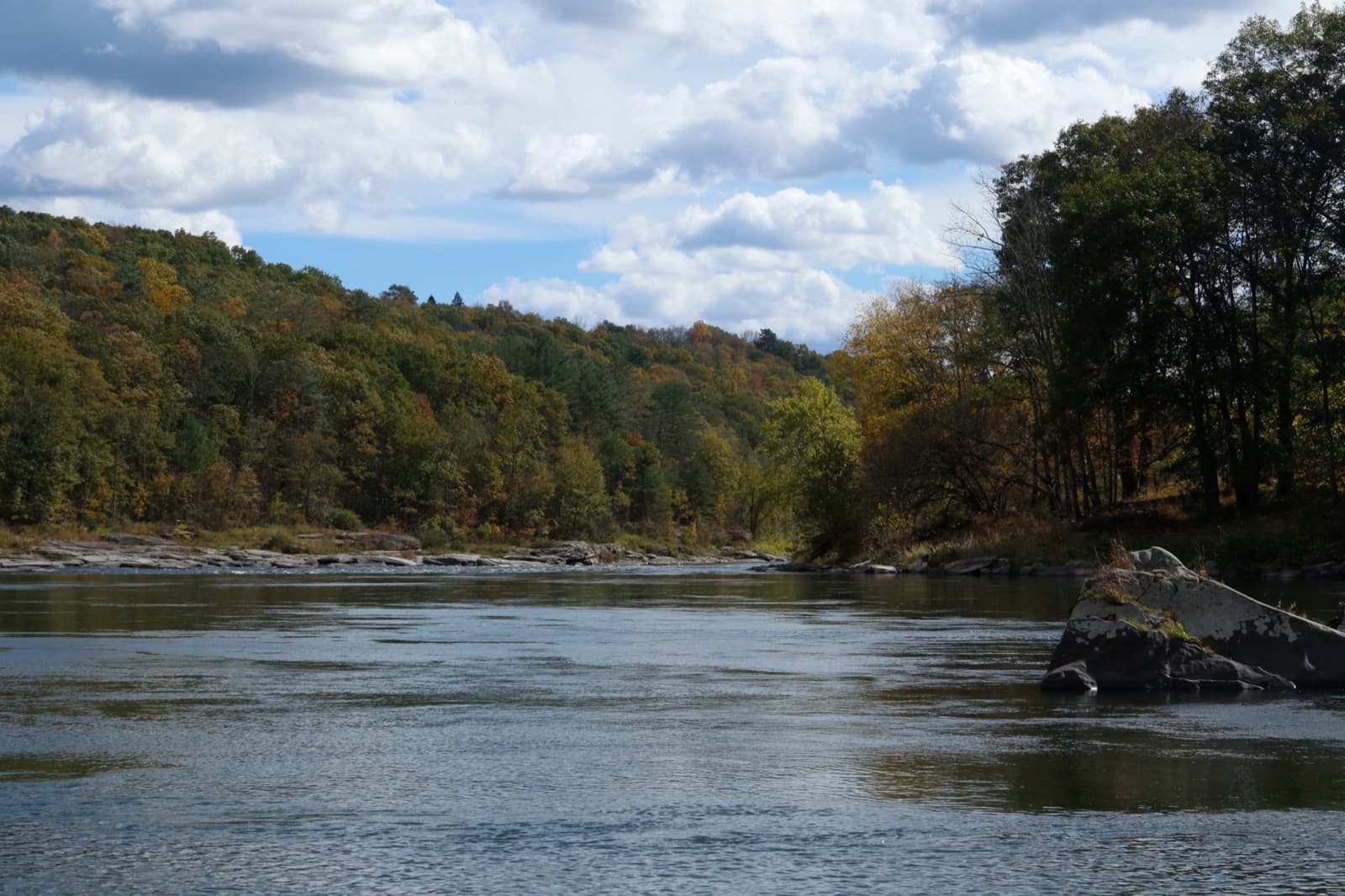 A wide river between forested hills, green with the first orange and red leaves