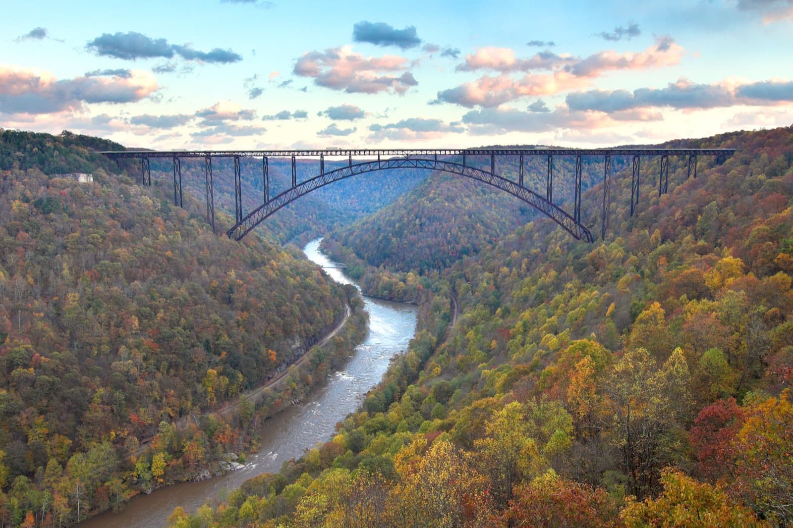 A steel arch bridge high over a river winding through hillsides of orange, yellow and green trees