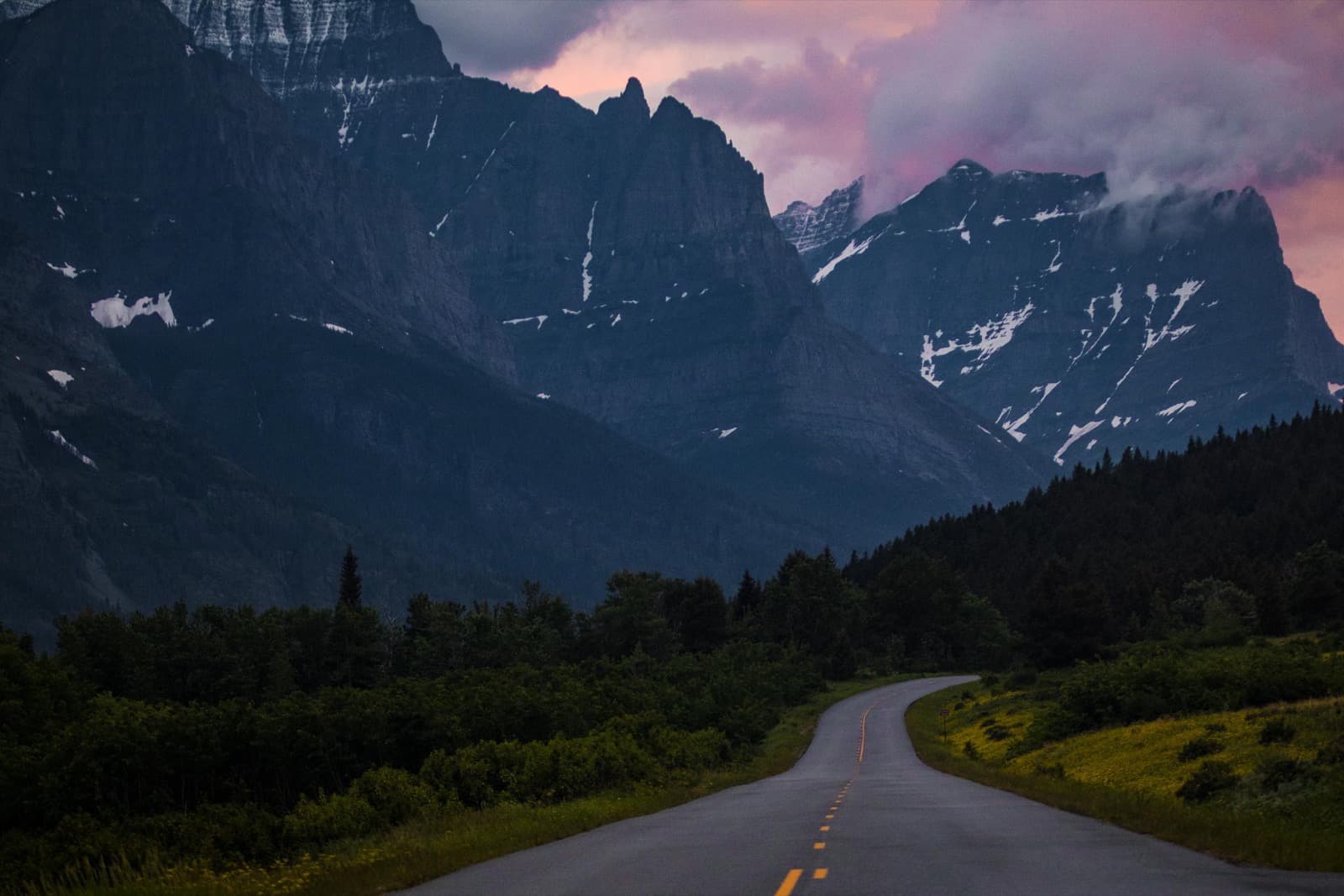 Jagged peaks rising above a forested valley, with an empty road curving into the distance