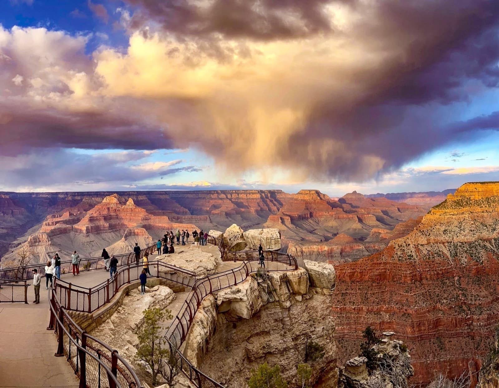 Swirling rain clouds at sunset above a vast canyon of colorful peaks and cliff walls