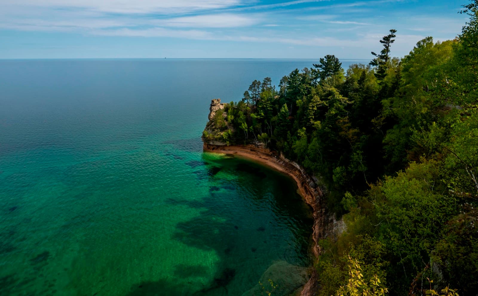 A sandstone rock formation rises out of blue-green Lake Superior on a sunny day