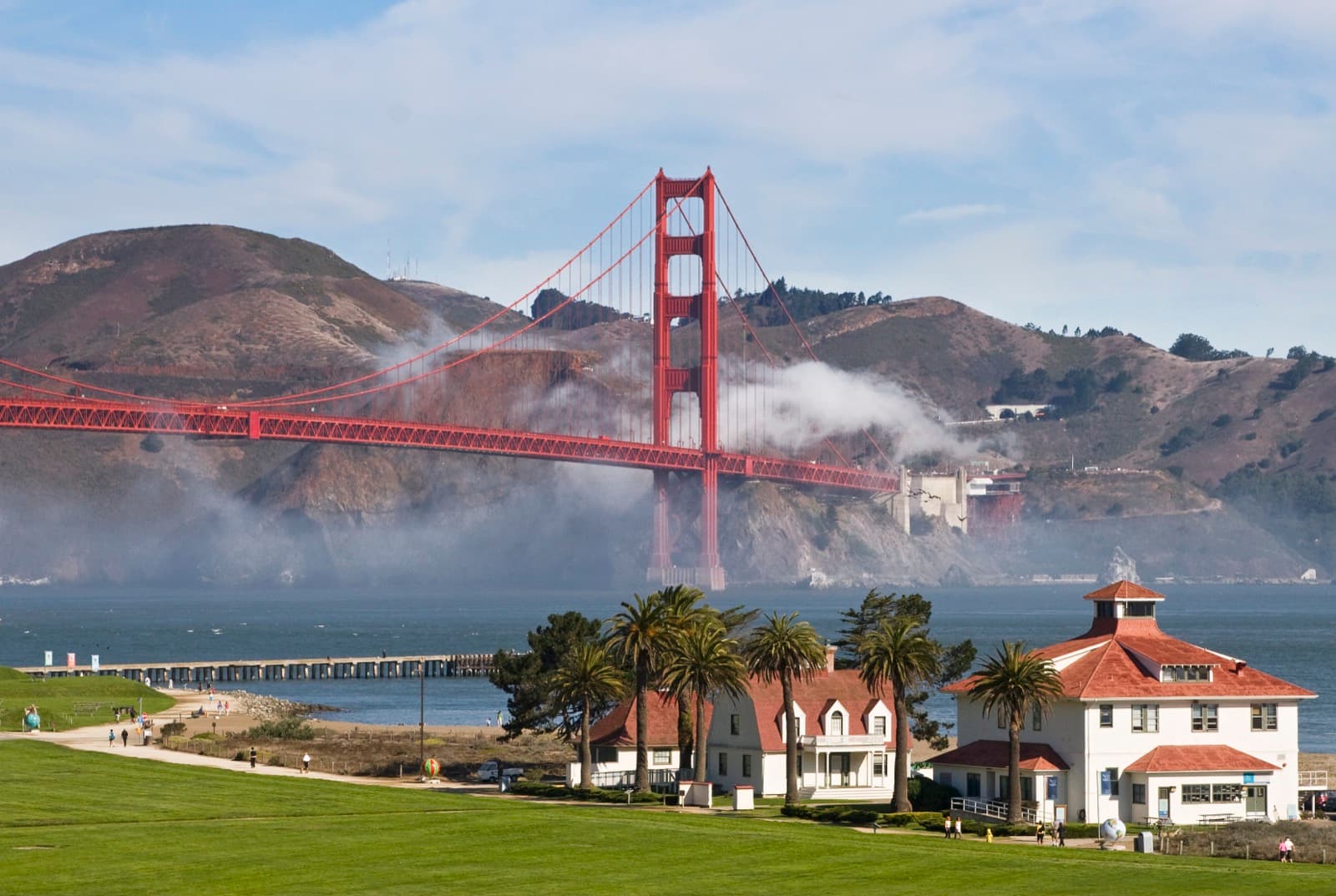White buildings with red roofs at Crissy Field with blue bay and Golden Gate Bridge and fog behind