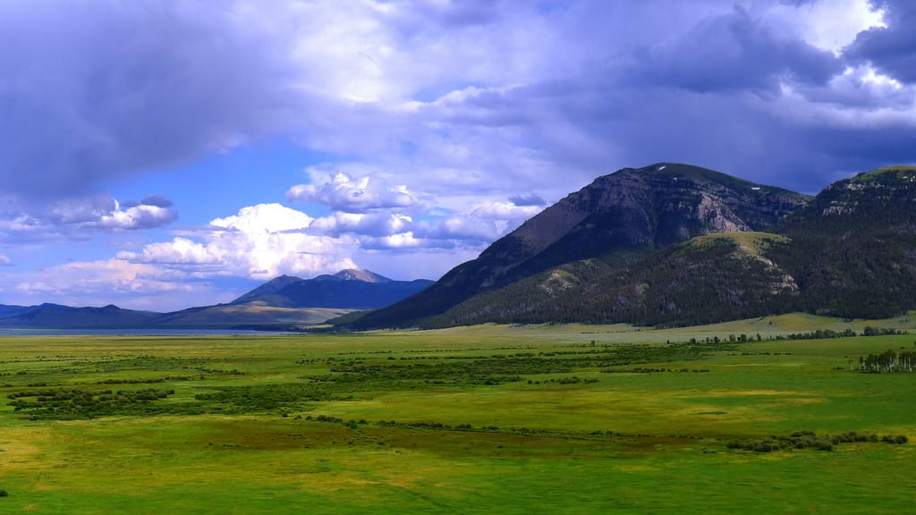 A wide green valley below a dark mountain and distant peaks under purple-gray clouds
